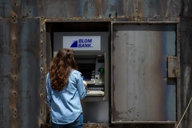 Una donna preleva da un bancomat a Beirut, nel Libano. Il bancomat è protetto da lastre di ferro per evitare vandalismi (AP Photo/Hassan Ammar)