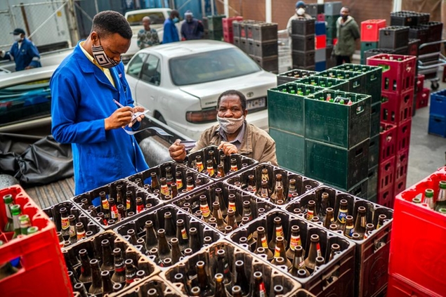 A liquor store employee checks returned beer bottles brought by a tavern owner at a Johannesburg hyper store Tuesday, Aug. 18, 2020. South Africa, which had one of the world's strictest anti-coronavirus lockdowns for five months, relaxed its restrictions Tuesday to permit the sales of alcohol and cigarettes and other returns to more ordinary life in response to decreasing new cases and hospitalizations for COVID-19.(AP Photo/Jerome Delay)
