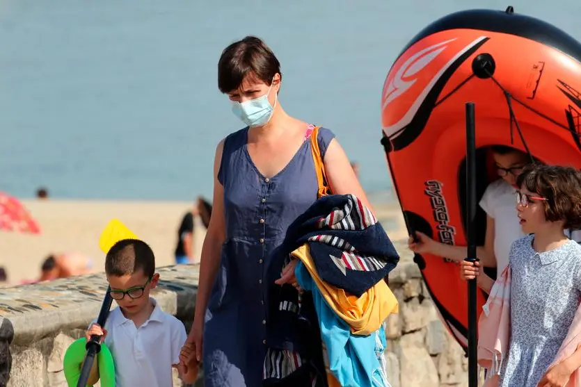 A woman wearing face masks to protect against coronavirus walks with her children along the beach in Saint Jean de Luz, southwestern France, Tuesday, July 27, 2021.Local authorities in France are re-imposing mask mandates and other virus restrictions because of fast-growing infections with the delta variant, which is causing COVID-19 hospitalizations in France to rise again. (AP Photo/Bob Edme)