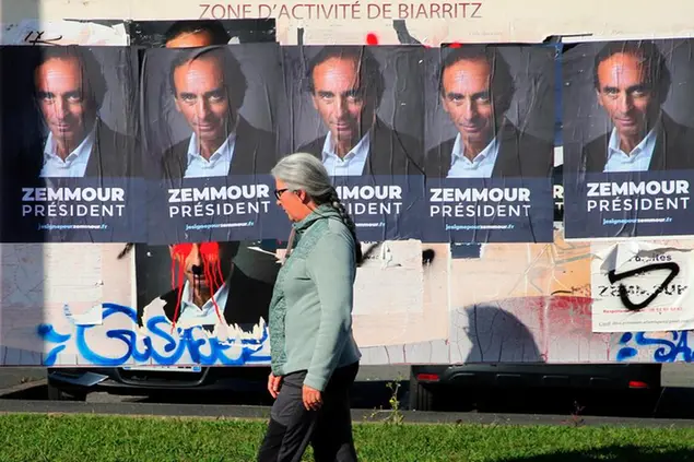 A woman walks past posters showing hard-right political talk-show star Eric Zemmour in Biarritz, southwestern France, Tuesday, Oct. 26, 2021. Provocative anti-immigration commentator Eric Zemmour is drawing national attention in France as he floats a possible presidential bid that could shake up the campaign for the April election.( AP Photo/Bob Edme)