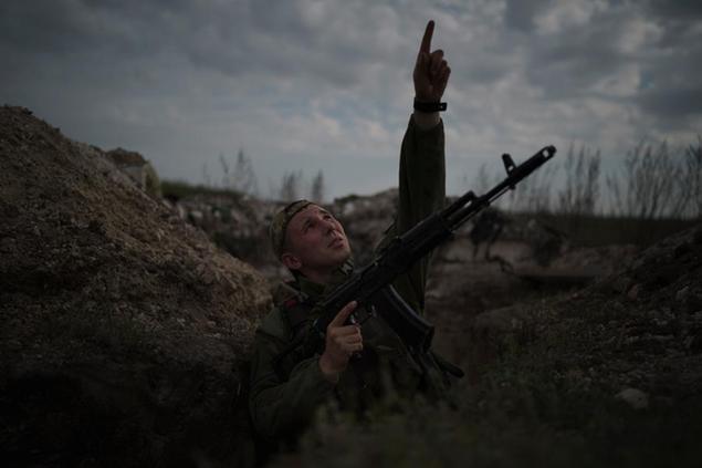 A Ukrainian soldier points at a passing helicopter as he stands in a trench on the line of separation from pro-Russian rebels near Donetsk, Ukraine, Monday, May 3, 2021. (AP Photo/Felipe Dana)