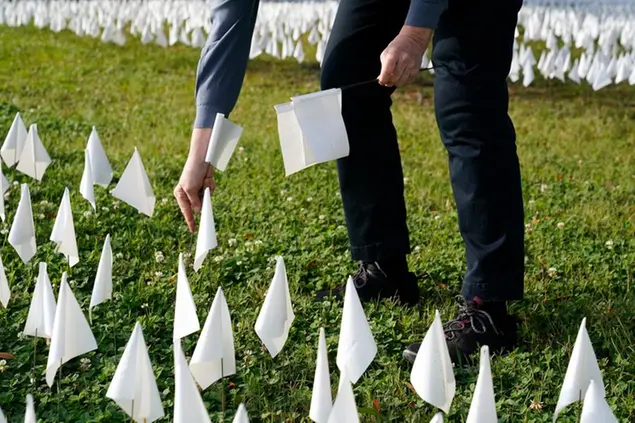 A volunteer adds white flags to a temporary art installation in remembrance of Americans who have died of COVID-19, Tuesday, Oct. 27, 2020, near Robert F. Kennedy Memorial Stadium in Washington. Artist Suzanne Brennan Firstenberg's installation, called \\\"In America, How Could This Happen,\\\" will include an estimated 240,000 flags when completed. (AP Photo/Patrick Semansky)