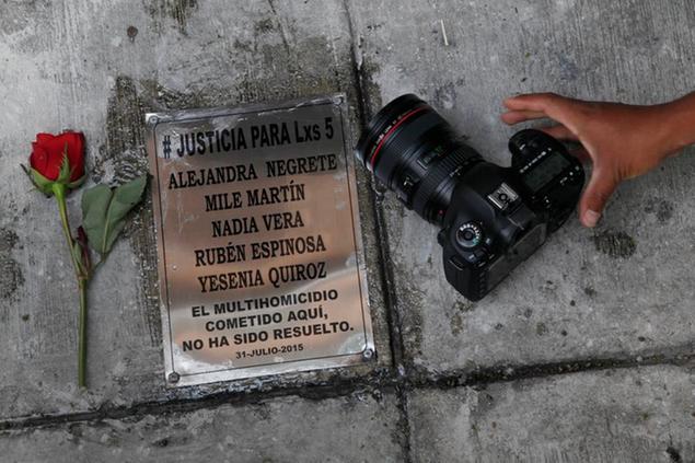 A photographer places his camera next to plaque with the names of photojournalist Ruben Espinosa and four women murdered with him in an apartment of Mexico City in 2015, during the first anniversary of their deaths, Sunday, July 31, 2016. Espinosa, worked for the investigative magazine Proceso and other media in Mexican state of Veracruz at the time of the murder. (AP Photo/Marco Ugarte)