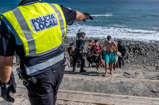 (Migranti sorvegliati dalla polizia spagnola dopo essere sbarcati sulla costa delle isole Canarie. Foto LaPresse)