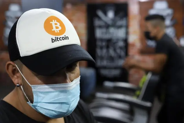 An employee wears a cap with the Bitcoin symbol at a barber shop in Santa Tecla, El Salvador, Saturday, Sept. 4, 2021. Starting Tuesday, Sept. 7, all businesses will have to accept payments in Bitcoin, except those lacking the technology to do so. (AP Photo/Salvador Melendez)