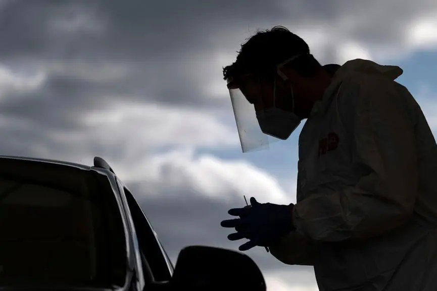 Staff at the COVID-19 test station stands with a swab at a car and explains the coronavirus test to the driver in Stuttgart, Germany, Friday, Oct. 9, 2020. (Marijan Murat/dpa via AP)