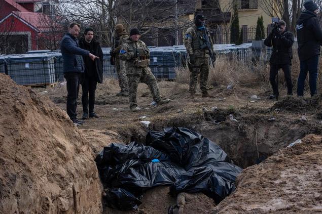 FILE - People stand next to a mass grave in Bucha, on the outskirts of Kyiv, Ukraine, April 4, 2022. AP journalists saw dozens of bodies in Bucha, many of them shot at close range, and some with their hands tied behind them. (AP Photo/Rodrigo Abd, File)