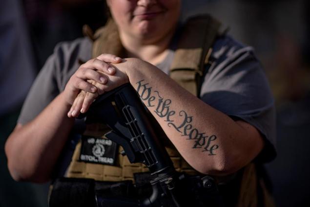 The tattoo \\\"We The People\\\", a phrase from the United States Constitution, decorates the arm of Trump supporter Michelle Gregoire as she rests her hand on her gun during a protest over the election results outside the central counting board at the TFC Center in Detroit, Friday, Nov. 6, 2020. (AP Photo/David Goldman)