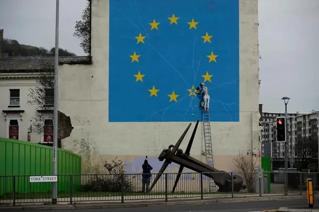 A man takes a photograph of a mural by street artist Banksy, depicting a star being chiselled from the European flag in Dover, south-east England, Monday, Jan. 7, 2019. Britain is testing how its motorway and ferry system would handle a no-deal Brexit split from the European Union by sending a stream of trucks from a regional airport to the port of Dover. (AP Photo/Matt Dunham)