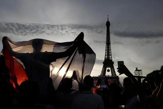 FILE - A supporter displays a French flag in the Paris fan zone in front of the Eiffel Tower during the Euro 2016 final soccer match between Portugal and France, Sunday, July 10, 2016 in Paris. Paris has decided not to display the matches of the World Cup in Qatar on giant screens in fan zones amid concerns over rights violations of migrant workers and the environmental impact of the tournament that have led some other French cities to make the same decision.(AP Photo/Laurent Cipriani, File)