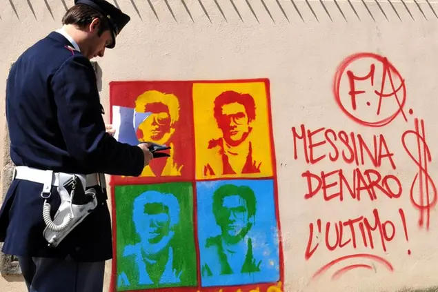 An Italian Police officer in Palermo, Sicily, southern Italy, Thursday April 24, 2008 looks on at graffiti on the perimeter wall of the city's cathedral, portraying Matteo Messina Denaro, a fugitive Mafia boss from the city of Trapani, in western Sicily. Denaro, who has been on Italy's wanted list since 1993 for murder and other crimes, is believed to be vying to succeed arrested Mafia boss Bernardo Provenzano. Writing at right of the dollar sign, says: \\\"Messina Denaro The Last One!\\\" (AP Photo/Alessandro Fucarini)