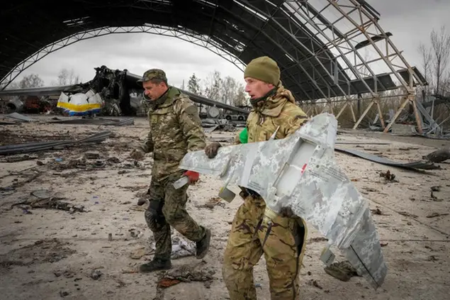 Ukrainian sappers carry a Russian military drone backdropped by the Antonov An-225, world's biggest cargo aircraft destroyed by the Russian troops during recent fighting, at the Antonov airport in Hostomel, on the outskirts of Kyiv, Ukraine, Monday, April 18, 2022. (AP Photo/Efrem Lukatsky)