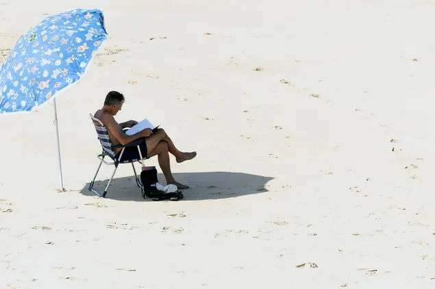 Un mano in spiaggia mentre legge un librio