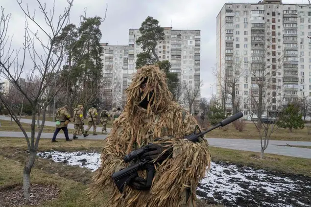 Ukrainian Territorial Defence Forces members walk past the city park as a camouflaged soldier stands in foreground, in the outskirts of Kyiv, Ukraine, Wednesday, March 9, 2022. Authorities announced a new ceasefire on Wednesday to allow civilians to escape from towns around the capital, Kyiv, as well as the southern cities of Mariupol, Enerhodar and Volnovakha, Izyum in the east and Sumy in the northeast. Previous attempts to establish safe evacuation corridors have largely failed due to attacks by Russian forces. (AP Photo/Efrem Lukatsky)