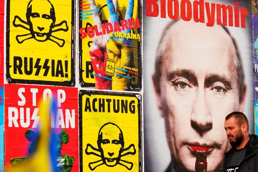 A man walks past a wall with posters depicting Russian President Vladimir Putin in Warsaw, Poland, on Thursday, March 24, 2022. Ukraine President Volodymr Zelenskyy called on people worldwide to gather in public Thursday to show support for his embattled country as he prepared to address U.S. President Joe Biden and other NATO leaders gathered in Brussels on the one-month anniversary of the Russian invasion. (AP Photo/Petr David Josek)