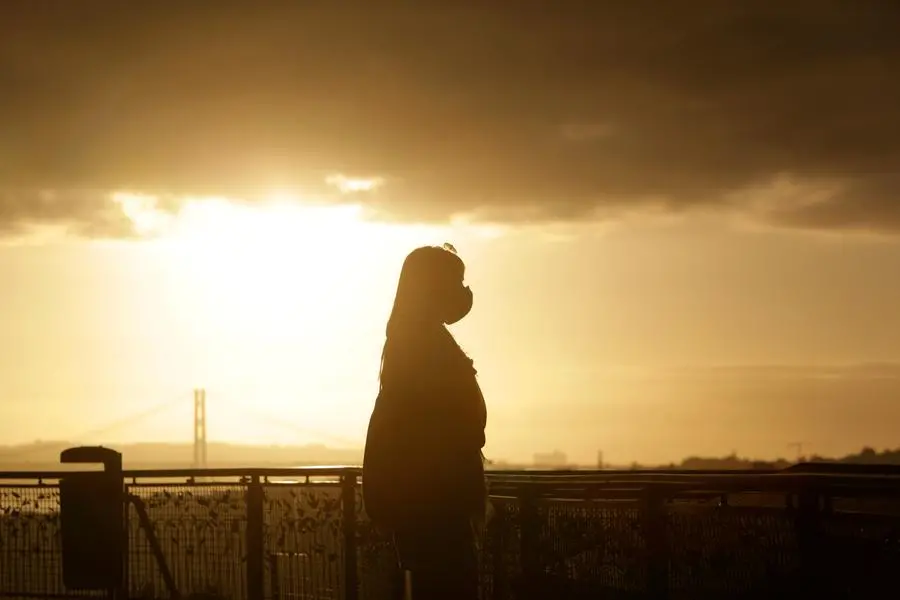 A woman wearing a face mask is silhouetted against the setting sun at a viewpoint overlooking Lisbon center, Monday, Dec. 21, 2020. (AP Photo/Armando Franca)