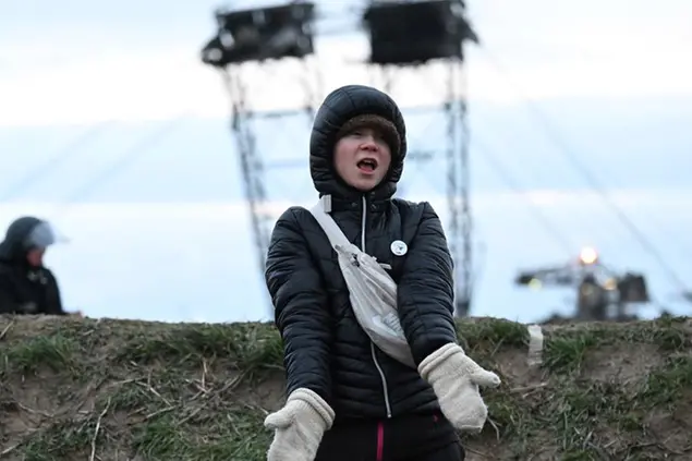 Climate activist Greta Thunberg stands between Keyenberg and L\\u00FCtzerath under police guard on the edge of the open pit mine and dances in Erkelenz, Germany, Sunday, Jan. 15, 2023. The energy company RWE wants to excavate the coal lying under Luetzerath, for this purpose, the hamlet on the territory of the city of Erkelenz at the opencast lignite mine Garzweiler II is to be demolished. (Federico Gambarini/dpa via AP)