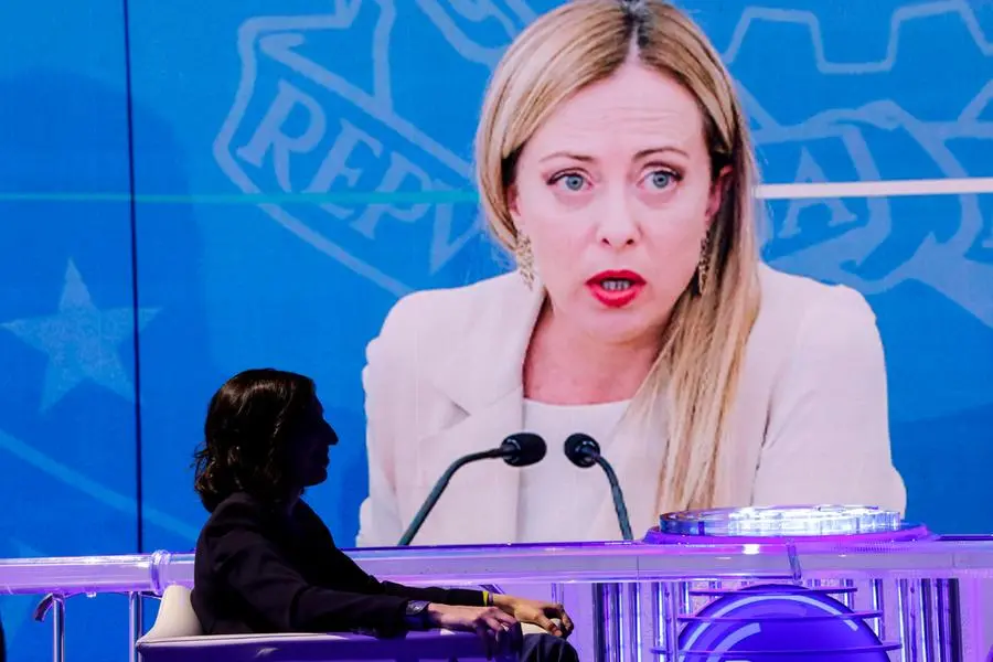 Elly Schlein in tv con la foto della premier Meloni sullo sfondo. Foto Ansa