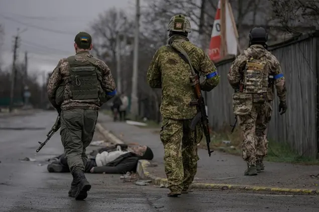 Ukrainian servicemen walk while checking bodies of civilians for booby traps, in the formerly Russian-occupied Kyiv suburb of Bucha, Ukraine, Saturday, April 2, 2022. As Russian forces pull back from Ukraine's capital region, retreating troops are creating a \\\"catastrophic\\\" situation for civilians by leaving mines around homes, abandoned equipment and \\\"even the bodies of those killed,\\\" President Volodymyr Zelenskyy warned Saturday. (AP Photo/Vadim Ghirda)