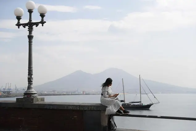 A woman types on the screen of her phone backdropped by the gulf of Naples, Italy, Tuesday, Sept. 15, 2020. (AP Photo/Gregorio Borgia)