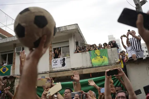 People watch the funeral procession of Brazilian soccer great Pele pass by the home of Pele's mother, where members of his family stand on the balcony, as his remains are taken from Vila Belmiro stadium to the cemetery in Santos, Brazil, Tuesday, Jan. 3, 2023. (AP Photo/Matias Delacroix)