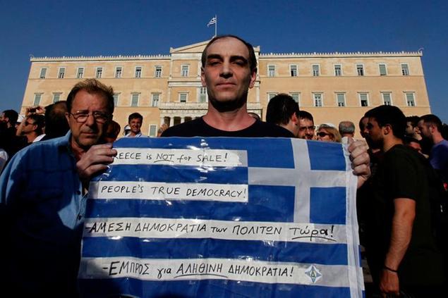 A protester holds a Greek flag in front of the Greek Parliament during a peaceful rally attended by thousands called through a social networking site - modeled on protests by young people in Spain, in central Athens, on Wednesday, May 25, 2011. The government in crisis-hit Greece has promised to privatize big part of the public sector in a massive sale of state assets aimed at raising 50 billion euros by the end of 2015, to help pay down the country's massive national debt. (AP Photo/Dimitri Messinis)