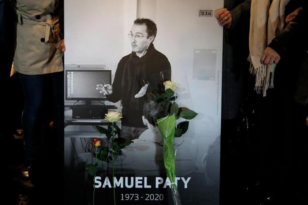 People hold a photo of the history teacher Samuel Paty , who was beheaded last week, during a memorial march in homage to him, Tuesday, Oct.20, 2020 in Conflans-Sainte-Honorine, northwest of Paris. Samuel Paty was beheaded on Friday by an 18-year-old Moscow-born Chechen refugee, who was later shot dead by police. Police officials said Paty had discussed caricatures of Islam's Prophet Muhammad with his class, leading to threats. (AP Photo/Lewis Joly)