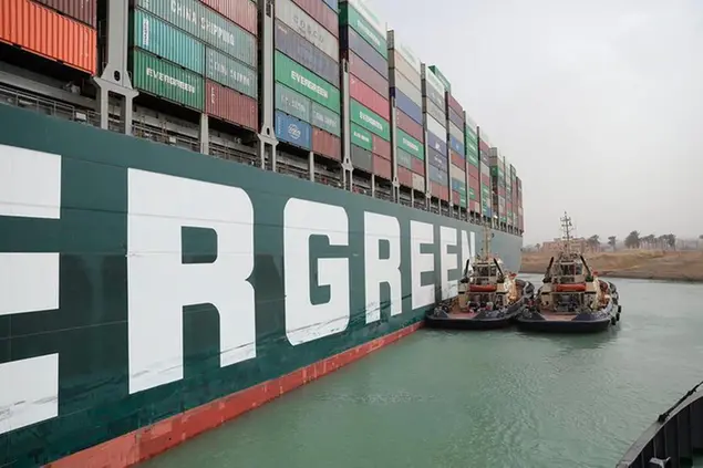 This photo released by the Suez Canal Authority on Thursday, March 25, 2021, shows two tugboats next to the Ever Given, a Panama-flagged cargo ship, after it become wedged across the Suez Canal and blocking traffic in the vital waterway from another vessel. An operation is underway to try to work free the ship, which further imperiled global shipping Thursday as at least 150 other vessels needing to pass through the crucial waterway idled waiting for the obstruction to clear. (Suez Canal Authority via AP)