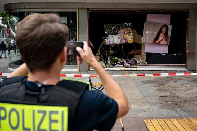 A policeman takes a photo of the damaged storefront at the scene of the fatal accident in Berlin, Germany, Thursday, June 9, 2022. On Wednesday June 8, a 29-year-old man drove his car into a group of students killing their teacher and crash into the store. (Fabian Sommer/dpa via AP)