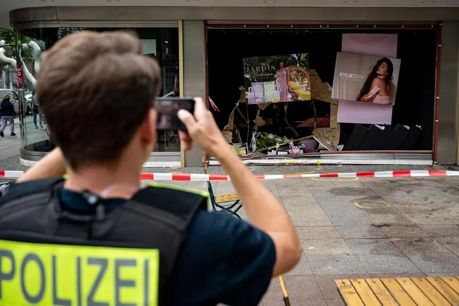A policeman takes a photo of the damaged storefront at the scene of the fatal accident in Berlin, Germany, Thursday, June 9, 2022. On Wednesday June 8, a 29-year-old man drove his car into a group of students killing their teacher and crash into the store. (Fabian Sommer/dpa via AP)