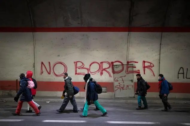 Migrants headed to France from Italy walk by a grafitti that reads \\\"No Border\\\" in a tunnel leading to the French-Italian border, Saturday, Dec. 11, 2021. As Europe erects ever more fearsome barriers against migration, volunteers along the Italy-France border are working to keep migrants from being killed or maimed by cold and mountain mishaps as they cross the high Alps. (AP Photo/Daniel Cole)