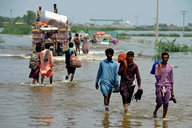 People wade through a flooded area of Sohbatpur, a district of Pakistan's southwestern Baluchistan province, Monday, Aug. 29, 2022. International aid was reaching Pakistan on Monday, as the military and volunteers desperately tried to evacuate many thousands stranded by widespread flooding driven by \\\"monster monsoons\\\" that have claimed more than 1,000 lives this summer. (AP Photo/Zahid Hussain)