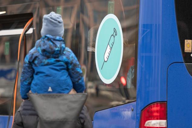 19 November 2021, North Rhine-Westphalia, Dortmund: A man with a child on his shoulders walks past a mobile vaccination centre in a bus parked in front of the German Football Museum. Photo by: Bernd Thissen/picture-alliance/dpa/AP Images