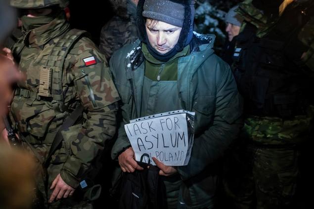 An asylum seeker from Syria who has been taken into custody by Polish border guards holds a paper saying \\\"I ask for asylum in Poland,\\\" in Harkawicze, Poland, on Wednesday Dec. 1, 2021. Poland in recent months has seen a large number of migrants from the Middle East enter its eastern border from Belarus, which is also the European Union's eastern frontier. The EU says it is part of a hybrid warfare on the part of the Belarusian government. (AP Photo/Michal Kosci)