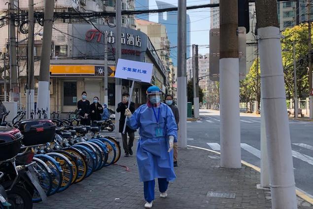 A worker in protective gear holds a sign which reads \\\"Do not crowd\\\" during a mass testing day for residents in a lockdown area in the Jingan district of western Shanghai Monday, April 4, 2022. China has sent more than 10,000 health workers from across the country to Shanghai, including 2,000 military medical staff, as it struggles to stamp out a rapidly spreading COVID-19 outbreak in China's largest city. (AP Photo/Chen Si)