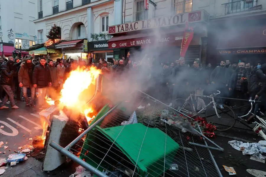 Members of Kurdish community stand next to a barricade on fire as they clash with police officers at the crime scene where a shooting took place in Paris, Friday, Dec. 23, 2022. Skirmishes erupted in the neighbourhood a few hours after the shooting, as members of the Kurdish community shouted slogans against the Turkish government, and police fired tear gas to disperse an increasingly agitated crowd. A shooting targeting a Kurdish cultural center in Paris Friday left three people dead and three others wounded. (AP Photo/Lewis Joly)