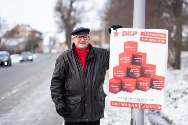 10 February 2021, Hessen, Reinheim: Arno Grieger (74) stands by an election poster of the German Communist Party (DKP) on an access road to the district of Ueberau. Since 1973, the retired teacher has sat without interruption in the town council of Reinheim in southern Hesse. There the 74-year-old today heads the DKP faction. (to dpa (\\\"\\\"The Red Village\\\" - Communist Tradition in the Municipality of Ueberau\\\") Photo by: Frank Rumpenhorst/picture-alliance/dpa/AP Images