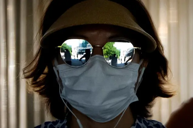 A woman wearing a face mask waits to cross an intersection in the central business district in Beijing, Thursday, July 7, 2022. (AP Photo/Mark Schiefelbein)