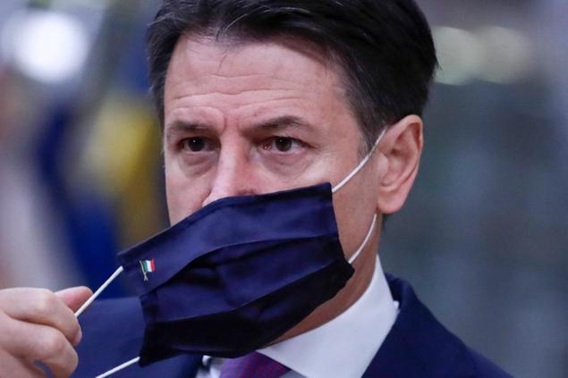 Italy's Prime Minister Giuseppe Conte takes off his protective mask as he arrives for an EU summit at the European Council building in Brussels, Friday, Oct. 2, 2020. European Union leaders will be assessing the state of their economy and the impact of the coronavirus pandemic on it during their final day of a summit meeting. (Olivier Hoslet, Pool via AP)