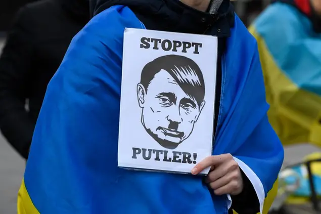 A demonstrator holds a sign with the inscription \\\"Stop Putler\\\" and the drawn likeness of Russia's President Putin, complemented with side parting and beard reminiscent of Hitler in Duesseldorf, Germany, Saturday, Feb. 26, 2022. Several hundred people demonstrated on Schadowplatz against Russia's attack on Ukraine. (Roberto Pfeil/dpa via AP)