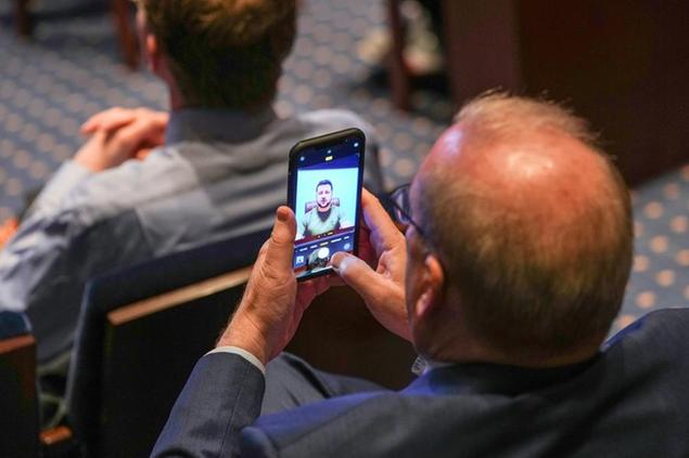 A member of Congress takes as photo as Ukraine President Volodymyr Zelensky speaks in a virtual address to Congress in the U.S. Capitol Visitors Center Congressional Auditorium in Washington, Wednesday, March 16, 2022. (Sarahbeth Maney/The New York Times via AP, Pool)