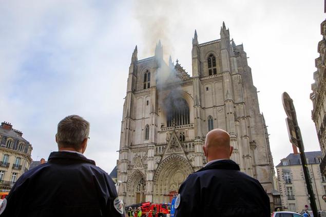 French police officers look at the blaze at the Gothic St. Peter and St. Paul Cathedral, in Nantes, western France, Saturday, July 18, 2020. The fire broke, shattering stained glass windows and sending black smoke spewing from between its two towers of the 15th century, which also suffered a serious fire in 1972. The fire is bringing back memories of the devastating blaze in Notre Dame Cathedral in Paris last year that destroyed its roof and collapsed its spire and threatened to topple the medieval monument. (AP Photo/Laetitia Notarianni)