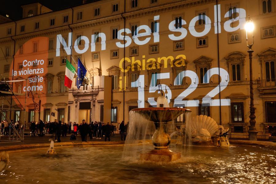 Una donna in piedi davanti a un gruppo di persone, con dati di disoccupazione e politiche di genere visibili in fondo