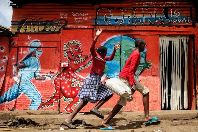 Children run down a street past a mural warning people about the dangers of the new coronavirus, in the Kibera slum of Nairobi, Kenya, on Wednesday, June 3, 2020. (AP Photo/Brian Inganga)