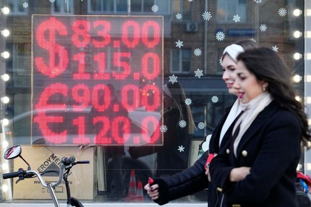 People walk past a currency exchange office screen displaying the exchange rates of U.S. Dollar and Euro to Russian Rubles in Moscow's downtown, Russia, Monday, Feb. 28, 2022. Ordinary Russians are facing the prospect of higher prices as Western sanctions over the invasion of Ukraine sent the ruble plummeting. That's led uneasy people to line up at banks and ATMs on Monday in a country that has seen more than one currency disaster in the post-Soviet era. (AP Photo/Pavel Golovkin)