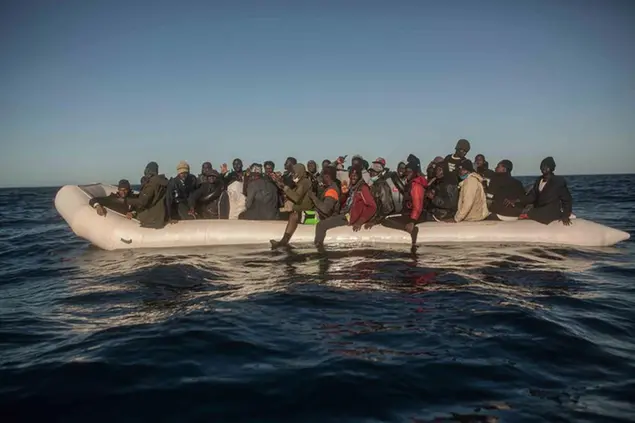 Migrants and refugees from different African nationalities react on an overcrowded rubber boat, as aid workers of the Spanish NGO Open Arms approach them in the Mediterranean Sea, international waters, off the Libyan coast, Saturday, Feb. 6, 2021. (AP Photo/Pablo Tosco)