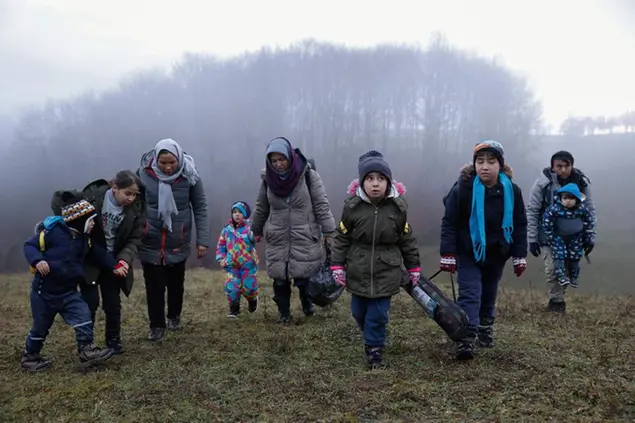Two Afghan families walk in a clearing after leaving a Croatian forrest near the Bosnian town of Velika Kladusa, Thursday Dec. 10, 2020. Entire migrant families are on the move in cold weather in Bosnia while trying to reach the West as the European Union warns the Balkan country it must act to prevent a humanitarian disaster. A statement by the EU Bosnia mission says current weather conditions are putting at risk the lives of more than 3,000 people sleeping rough or staying in inadequate conditions. (AP Photo/Marc Sanye)