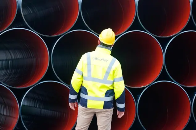 08 December 2022, Schleswig-Holstein, Brunsb'ttel: An employee stands in front of ETL 180 gas pipes at Gasunie Deutschland's pipe storage yard in Brunsb'ttel. The pipes are intended for laying the gas pipeline from the floating LNG terminal in Brunsb'ttel to Hetlingen in the Pinneberg district. A total of 3000 pipes are to be laid in the ground over a length of 55 kilometers by October 2023. Photo by: Marcus Brandt/picture-alliance/dpa/AP Images