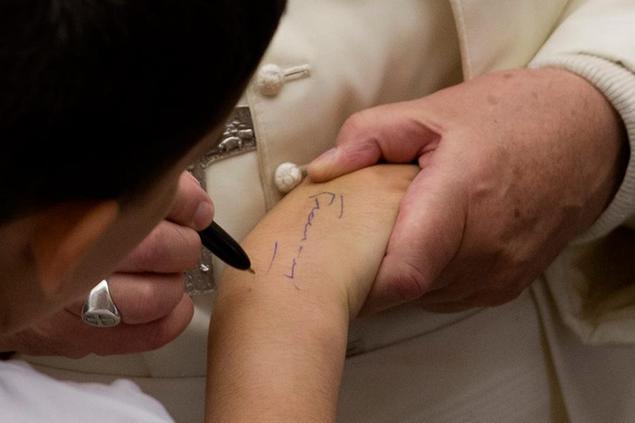 Pope Francis signs an autograph on the arm of a boy during a special Jubilee audience with poor people from the dioceses of Lyon, France, in the Pope Paul VI hall, at the Vatican, Wednesday, July 6, 2016. (AP Photo/Andrew Medichini)