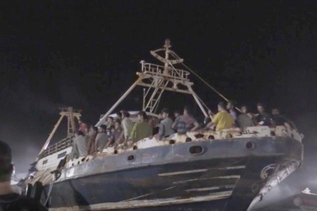 In this frame taken from video, a fishing boat with migrants is docked at the port of the Sicilian island of Lampedusa, southern Italy, late Monday, Sept. 27, 2021. A rusty, overloaded fishing boat carrying nearly 700 migrants arrived at an Italian island port amid fresh diplomatic efforts by Mediterranean governments to seek more European help in handling migrant flows. (AP Photo/Mauro Buccarello)